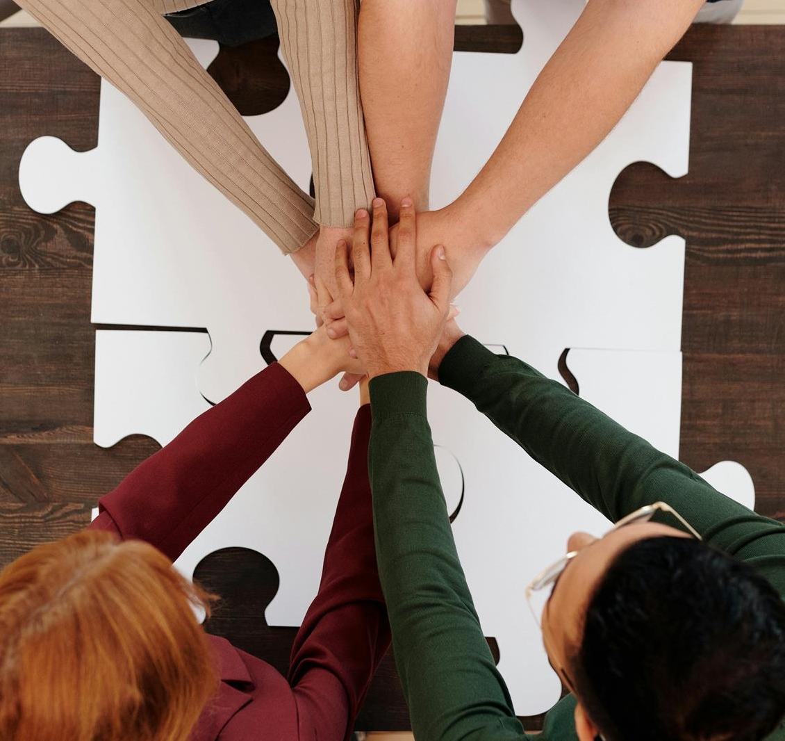 Hands of four colleagues stacked together over a table of puzzle pieces
